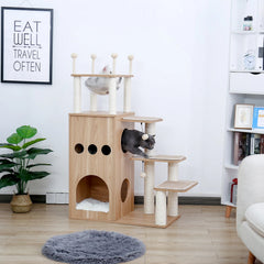 Cat climbing tree in a room with a plant and bookshelf.